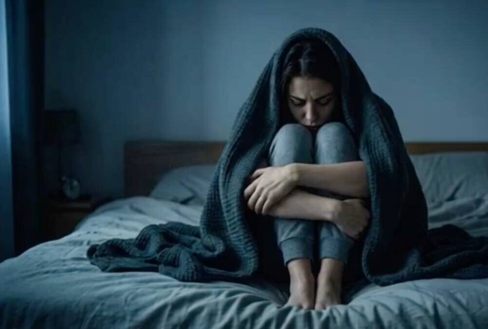 A woman wrapped in a dark blanket sitting curled up on a bed reflecting on why physical distance is not psychological freedom.